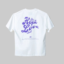 Load image into Gallery viewer, White t-shirt with purple text 'The Hopi Love Club' on a beige background