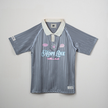 Load image into Gallery viewer, A vintage short-sleeve polo shirt with a gray and blue vertical striped pattern, featuring a cream collar, pink seashell graphics, and 'Hopi Love' printed in light blue and pink on the chest.