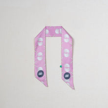 Load image into Gallery viewer, A pink silk scarf with a white and green geometric seashell pattern and circular motifs, laid flat on a light beige background.
