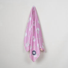 Load image into Gallery viewer, A pink silk scarf with a white seashell pattern and a small circular navy blue logo patch, hanging against a plain light gray wall.
