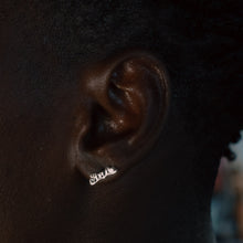 Load image into Gallery viewer, A close-up of a person's ear wearing a small silver script earring that reads 'Love'.
