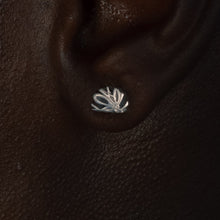 Load image into Gallery viewer, A close-up of a person's ear wearing a small silver earring with a leaf or fan-like cutout design, set against dark skin.

