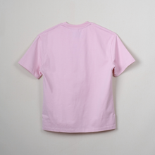 Load image into Gallery viewer, A light pink short-sleeve crewneck t-shirt shown from the back, hanging against a plain light gray wall.
